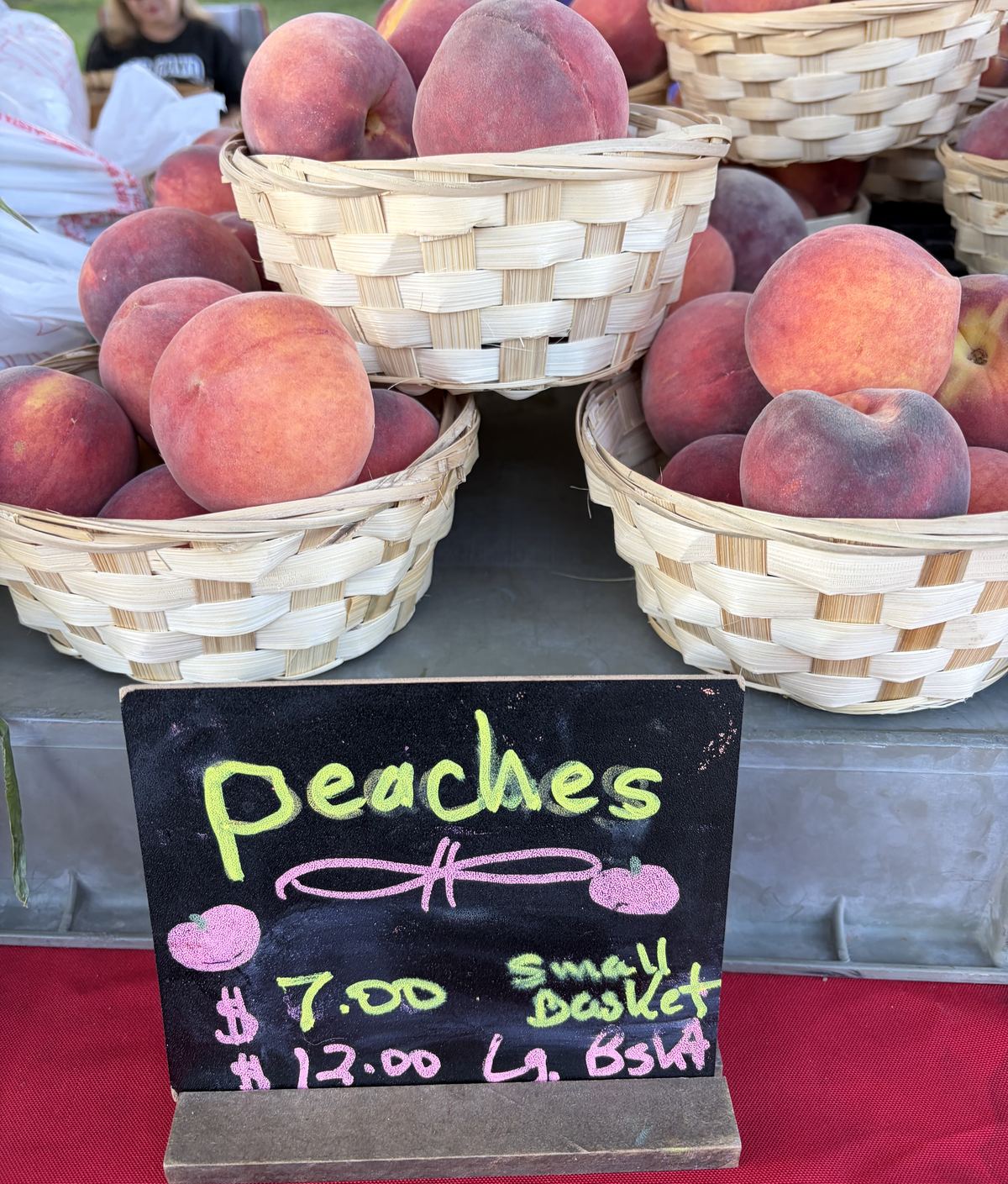 Baskets of ripe peaches beside a chalkboard reading Peaches $7 small basket, $12 large basket