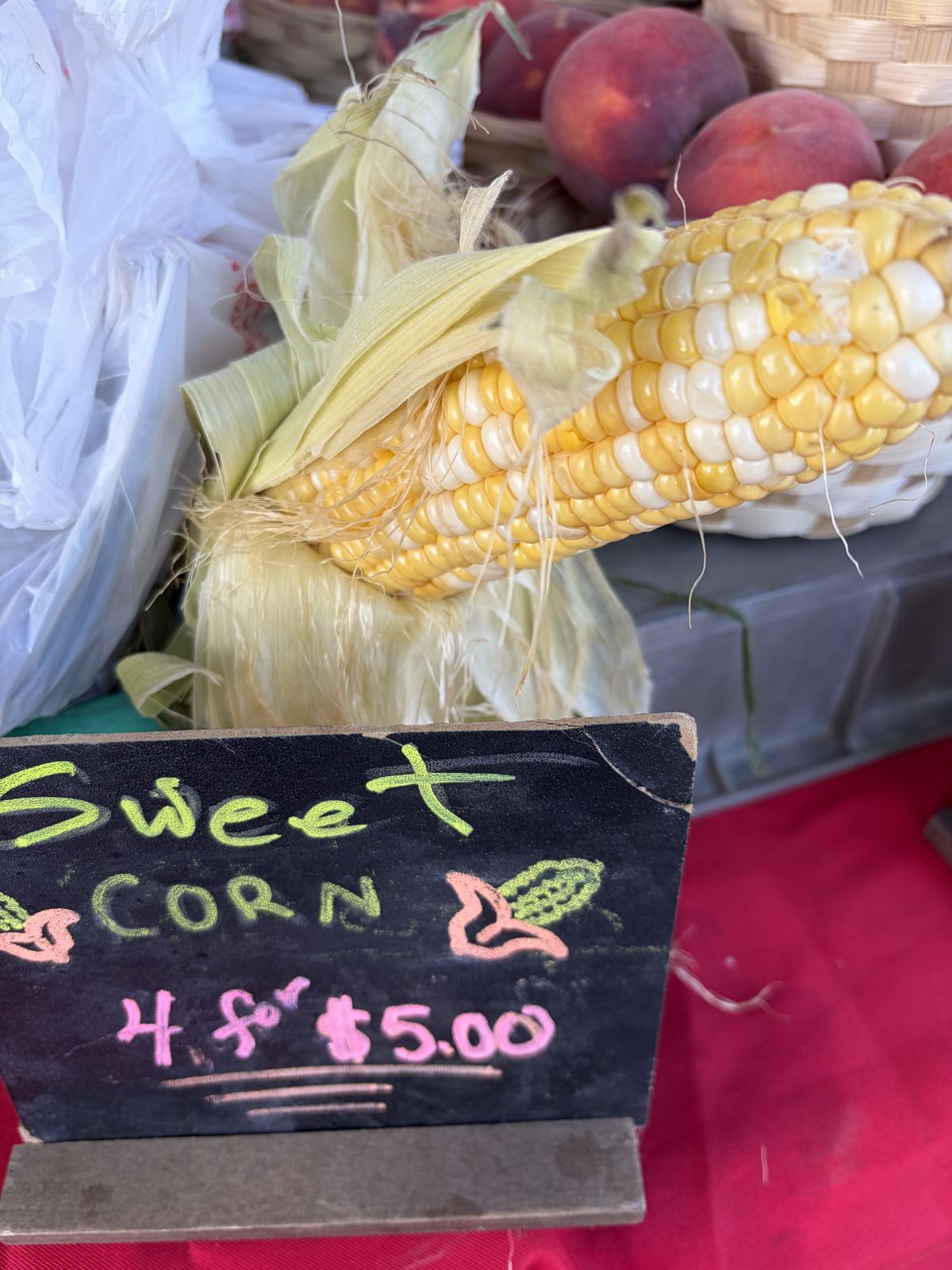 Ear of sweet corn beside a chalkboard reading Sweet Corn 4 for $5